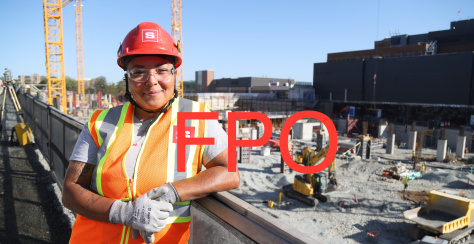 An apprentice poses in front of a job site.
